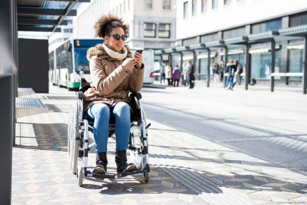 Woman in wheelchair looking at her smartphone at bus station